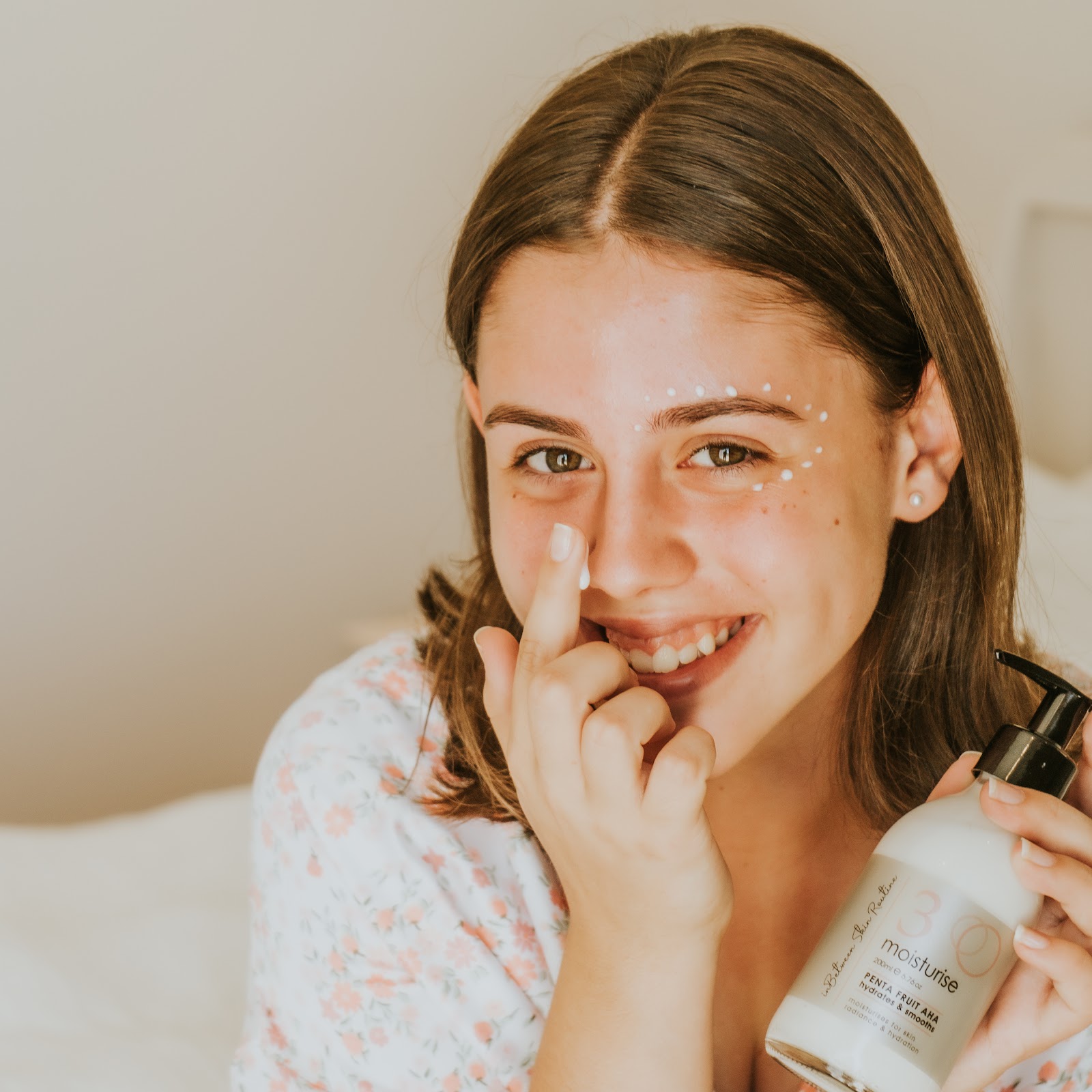 A young woman smiling as she applies In-Between moisturiser to her skin